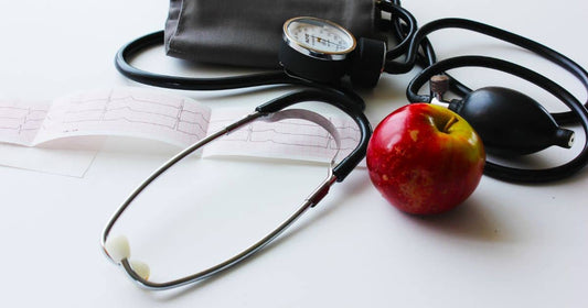 Blutdruckmessgerät, Apfel und EKG zeigen Gesundheitsfokus.