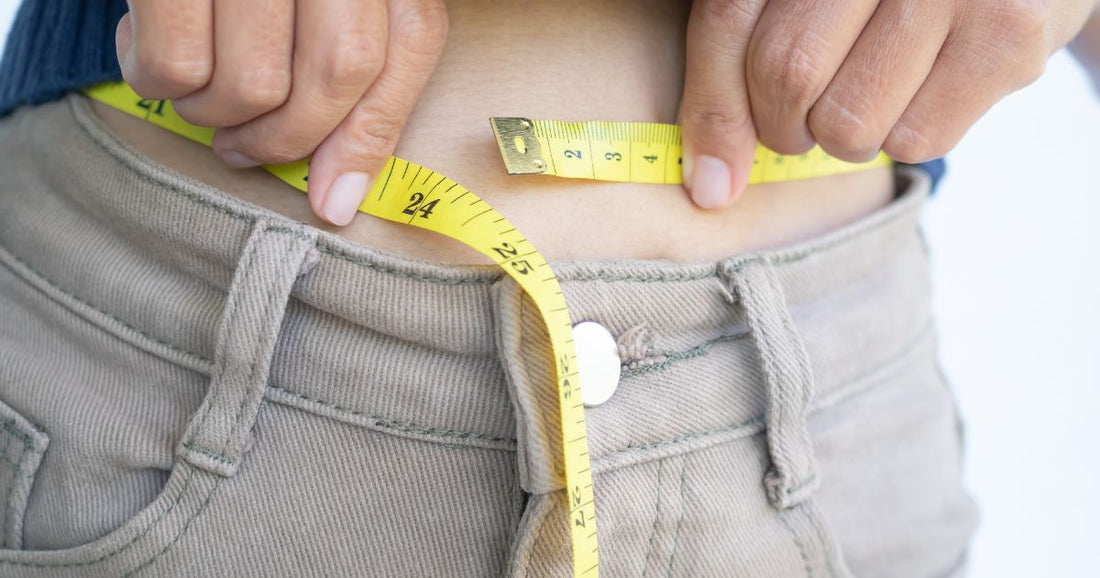 Person misst Taille mit Maßband zur Kontrolle des Gewichts.